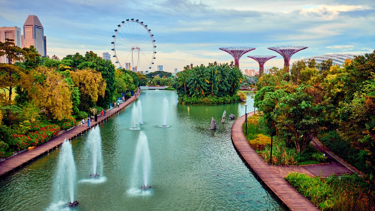 Gardens by the Bay in Singapore A lush park in Singapore featuring water fountains, the Singapore Flyer Ferris wheel, and futuristic Supertree structures surrounded by greenery.